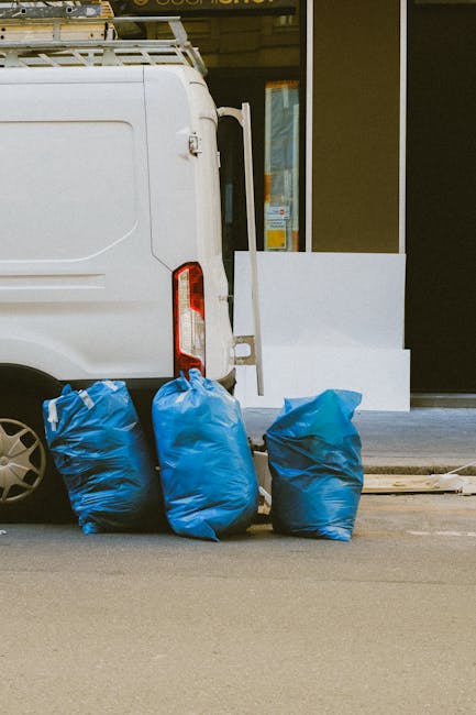 In this image, the rear section of a white commercial van is visible, positioned on an urban street pavement. The van features a vertical tail light on the right side and a partially visible sliding d